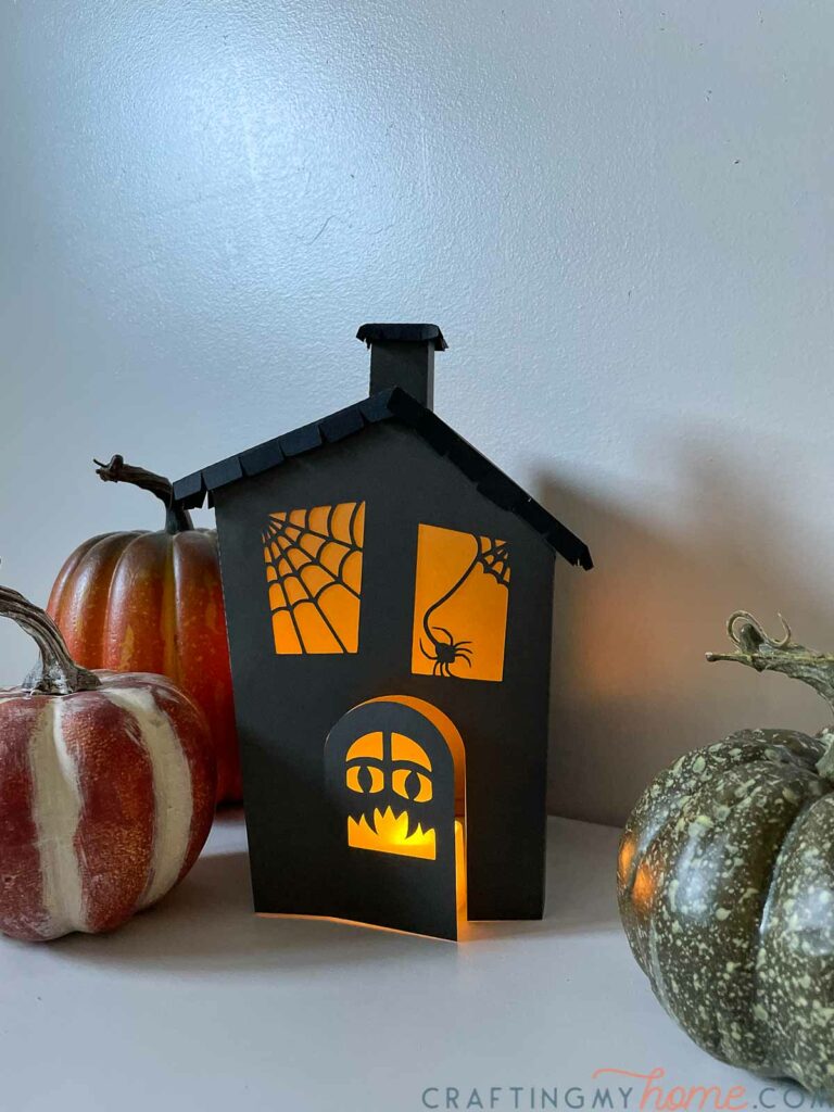 Front of the haunted house lantern with a monster face on the front door in dim light with a candle glow inside. 