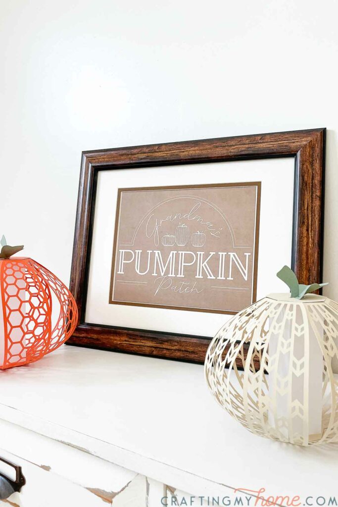 Framed pumpkin patch printable on a table next to decorative pumpkins. 
