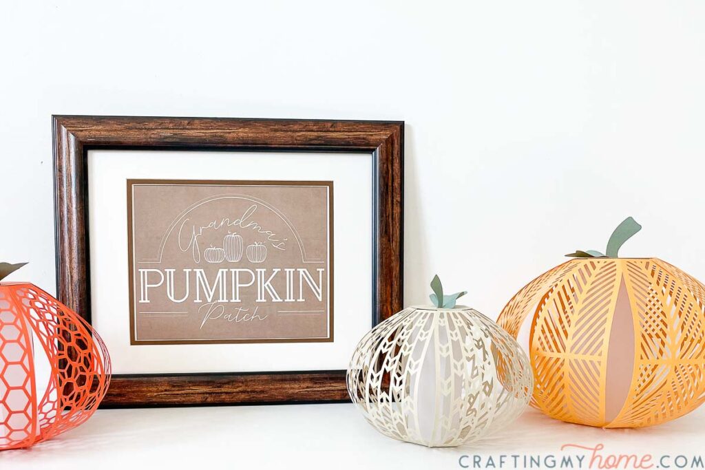 Seasonal printable for fall in a wood frame next to pumpkin lanterns. 