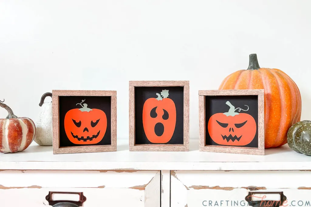 Three simple Halloween signs sitting on a white console table with pumpkins around it. 