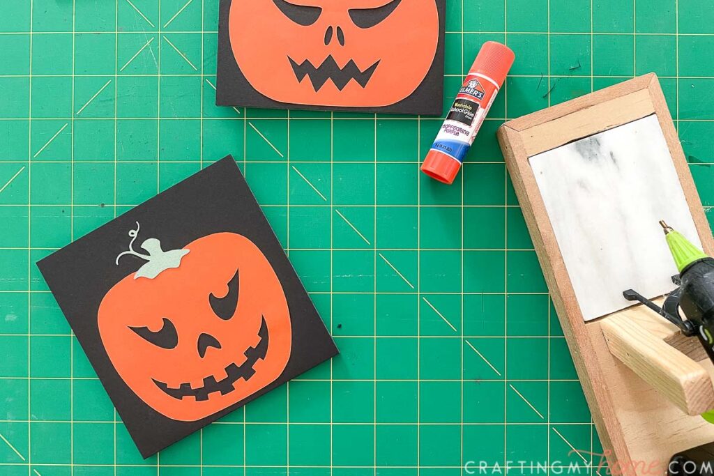 Glueing the paper jack-o-lantern to the back of the sign with a glue stick and a glue gun. 