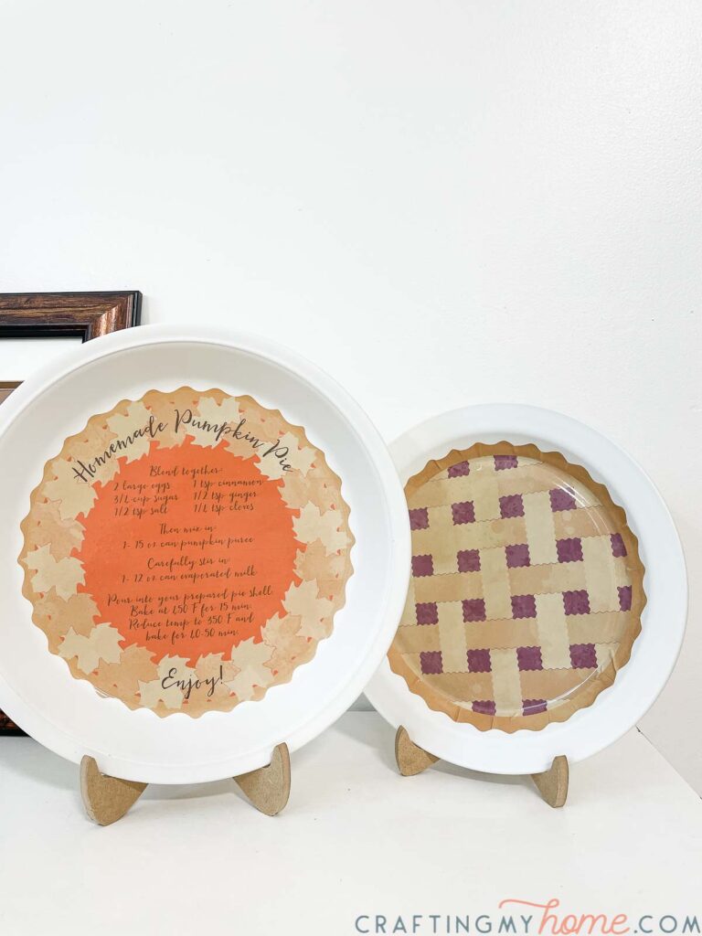 Two decorative pie plates, one of a pumpkin pie with a recipe and the other a lattices berry pie, in easels on a console. 