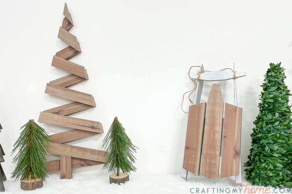 Winter vignette with rustic paper Christmas tree and decorative wooden sled around faux Christmas trees. 