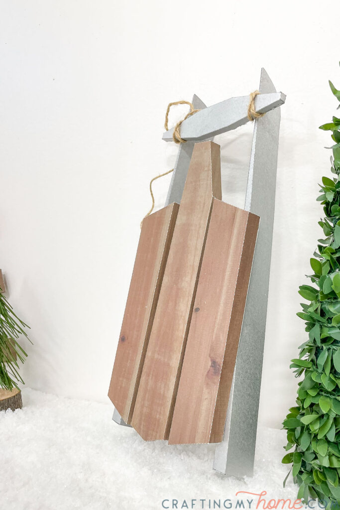 Side view of the decorative sled leaning up against a wall by a decorative tree. 