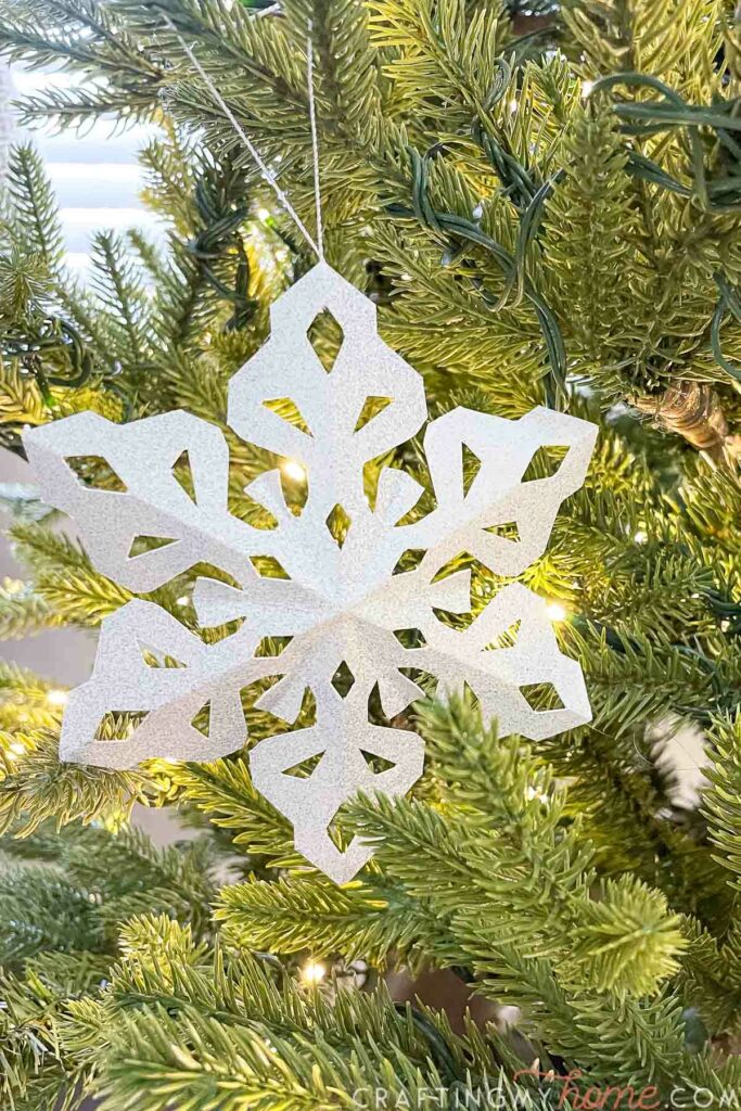 Close up of the paper snowflake ornament with glitter on it on a tree. 