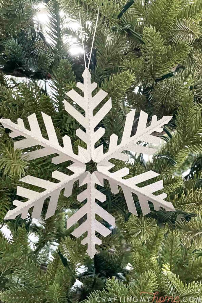 Fern-like 3D snowflake made from cardstock hanging on a Christmas tree.
