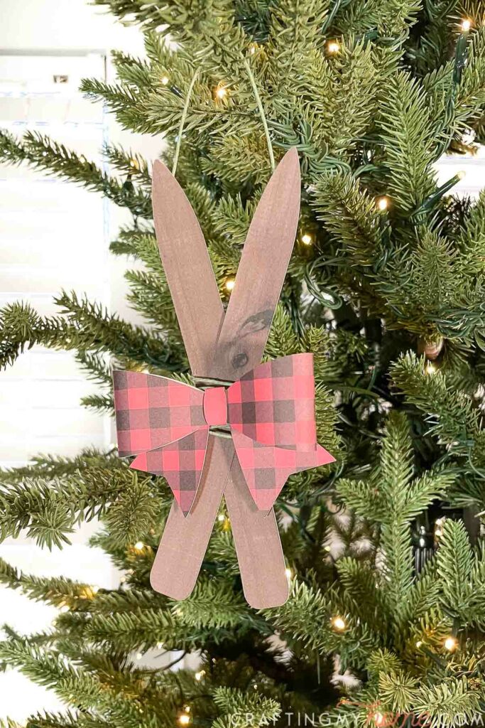 Paper Christmas ornament that looks like a set of wooden skis with a buffalo check bow on it. 