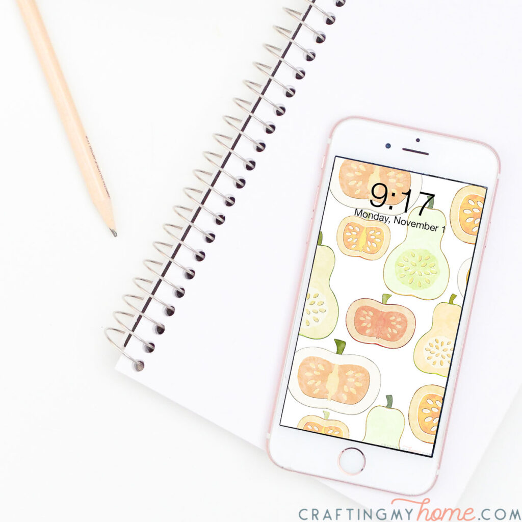 White iPhone with watercolor digital background of pumpkins and gourds on the lock screen. 