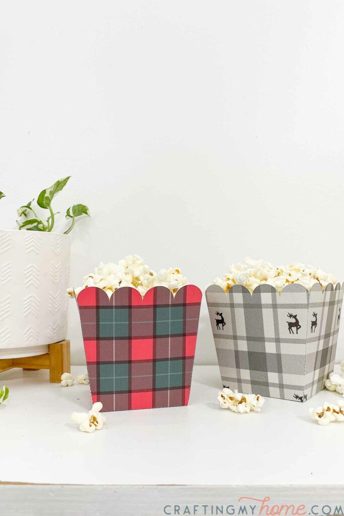 Tall square paper party trays with Christmas plaid prints on the outside and popcorn inside. 