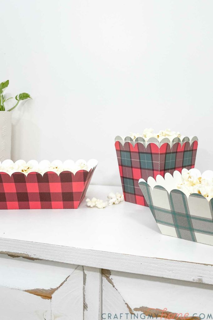 Two different sizes of plaid food trays with red and green prints on them filled with popcorn. 
