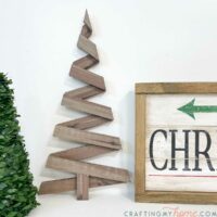 Rustic paper Christmas tree on a table next to a wood sign and faux tree.
