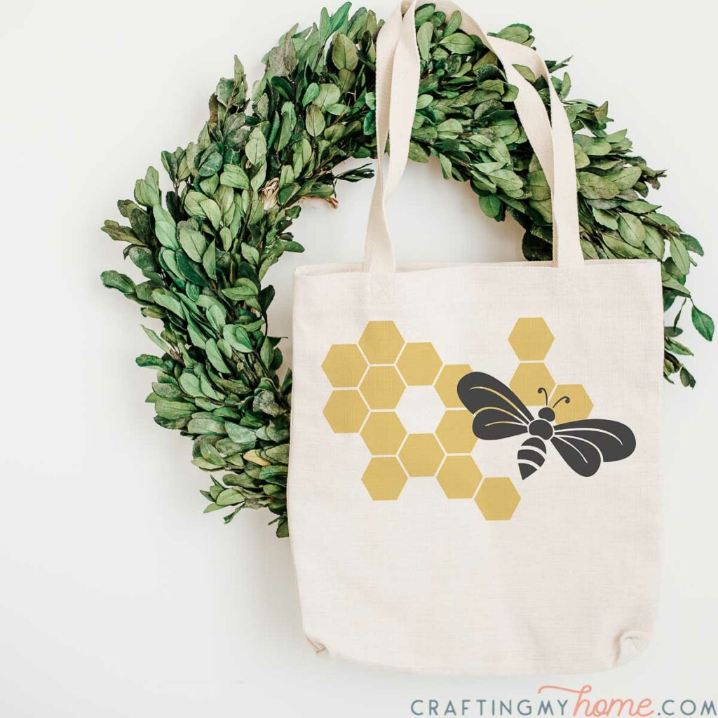 Canvas bag with bee SVG over honeycomb pattern in the front hanging on a wreath.