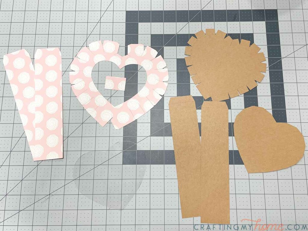 All the pieces needed to make your own heart box cut out and laying on a craft table. 