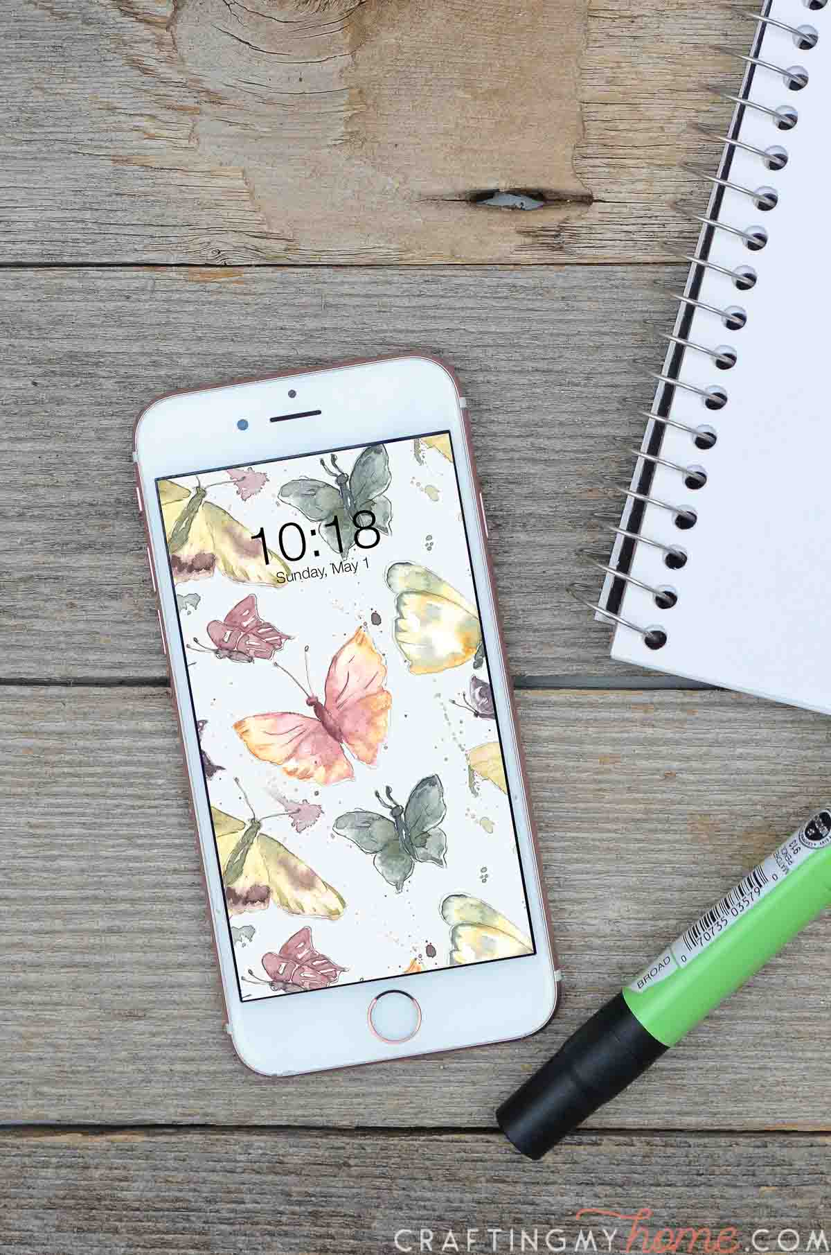 Watercolor butterfly digital wallpaper on a smartphone on a wood desk.