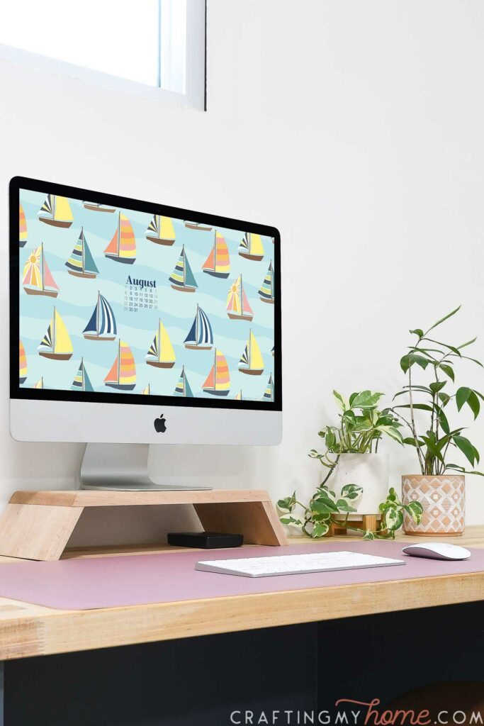 Desktop computer with the colorful sailboat patterned free digital wallpaper for August on the screen in a feminine office. 
