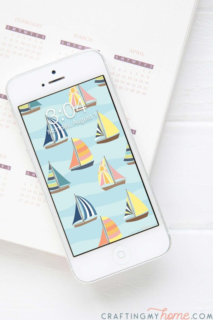 White iphone with a colorful sailboat digital wallpaper on the home screen sitting on a planner.