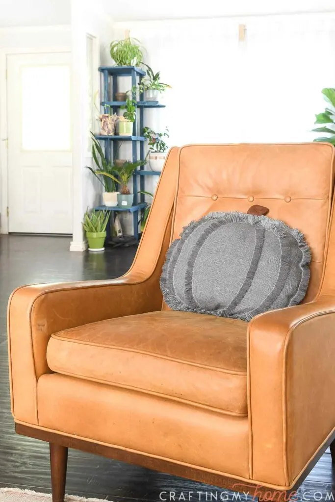 Camel colored leather chair with blue-gray cozy modern pumpkin pillow on it.