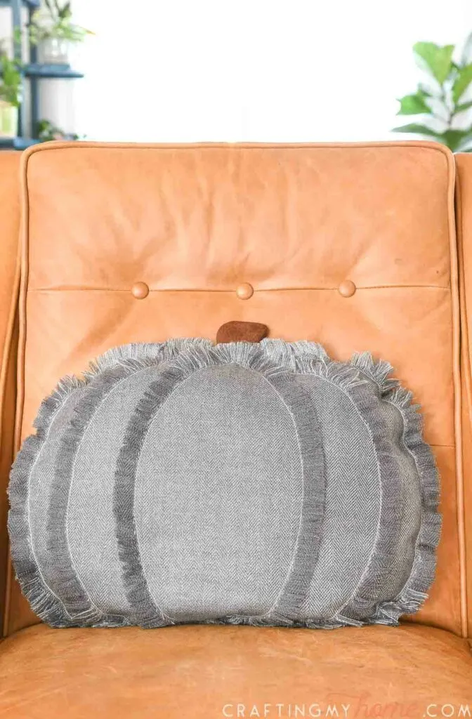 Pumpkin shaped throw pillow on a leather chair.