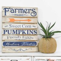 Cute pumpkin shaped planter next to stenciled farmers market sign.