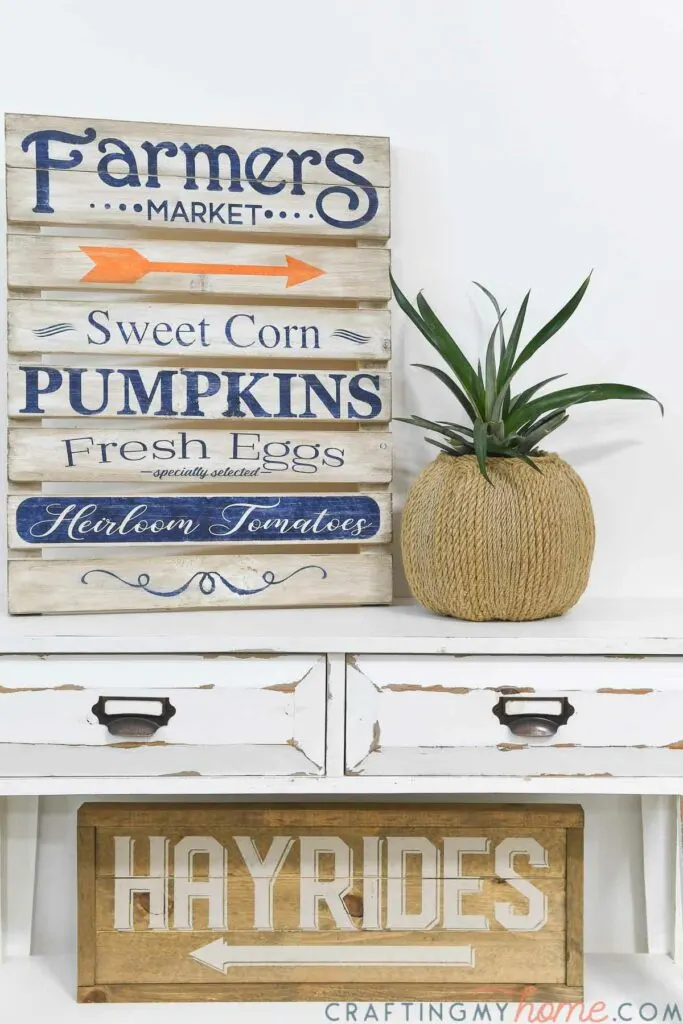 Fall vignette with pumpkin planter next to Farmers Market sign on a console above a wood hayrides sign. 