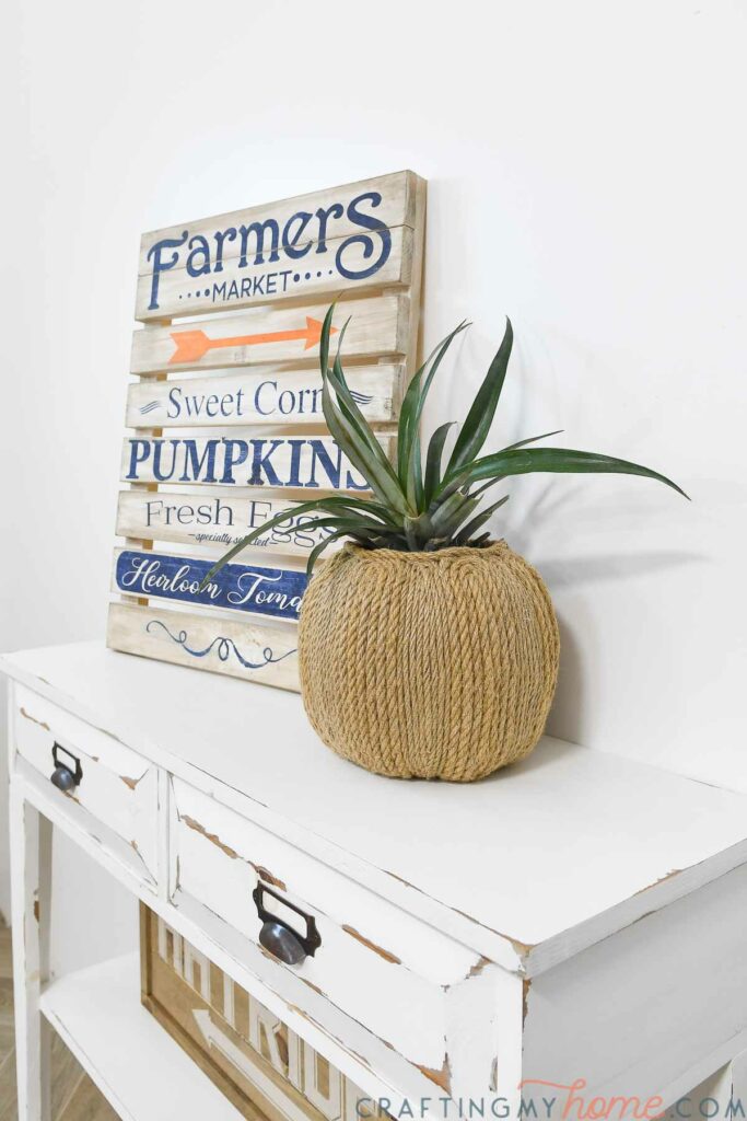 DIY pumpkin planter with plant inside it on a console table with other fall decor. 