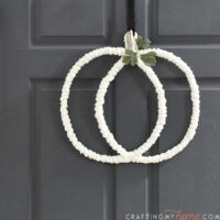 Cream wire pumpkin wreath with stem and leaf hanging on a charcoal front door.