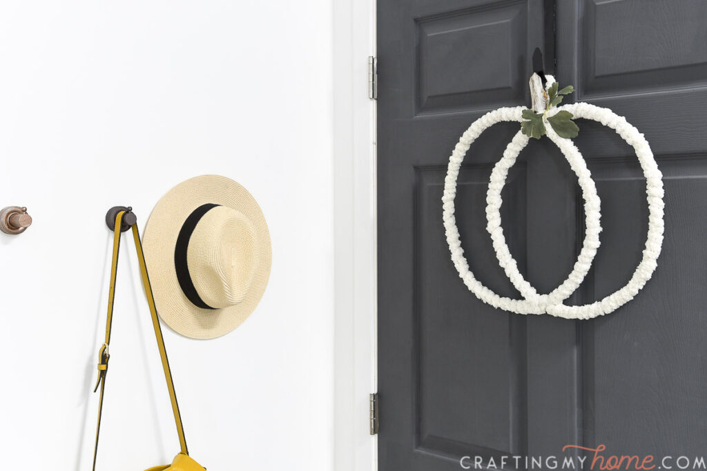 Entryway with hooks next to a black door with a modern white pumpkin wreath hanging on it. 
