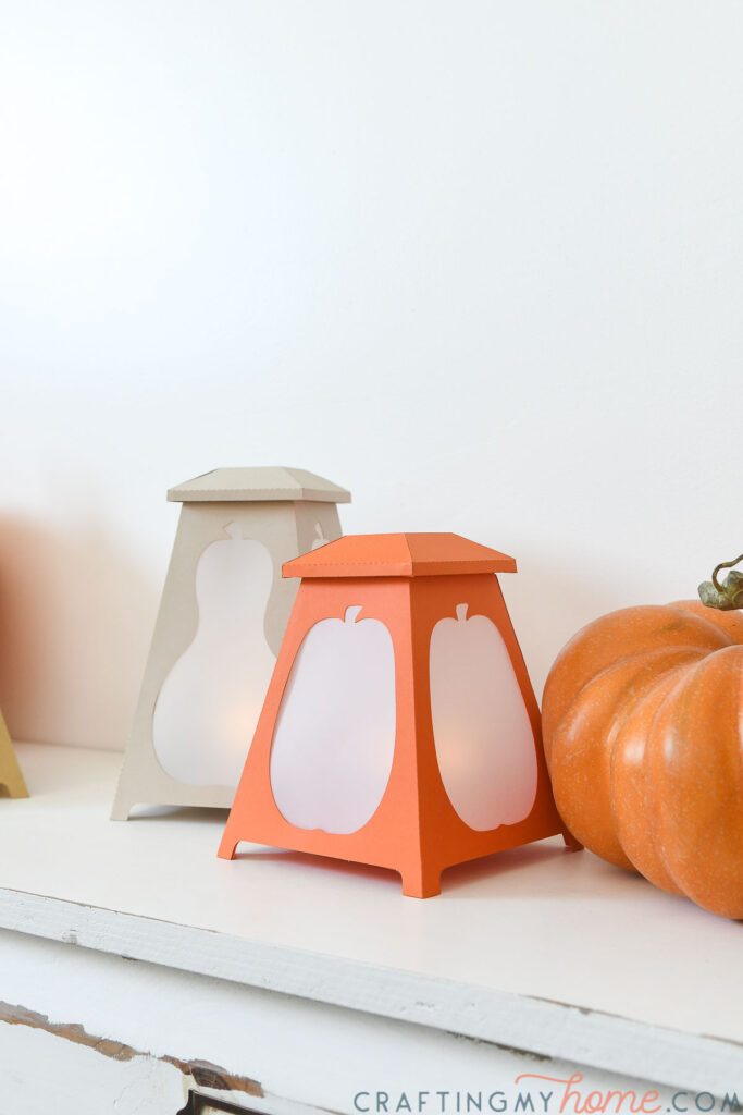 Orange and taupe paper lantern with pumpkin shapes in the sides. 