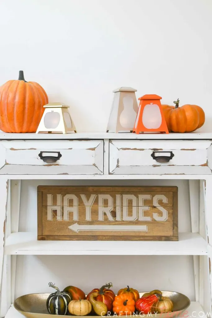 Fall vignette with DIY tapered fall lanterns, hayrides sign, and dish full of small pumpkins on a console table. 