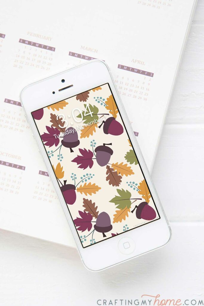 White iPhone with fall digital wallpaper on the screen sitting on a planner. 